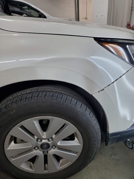White car's front fender with a dent, next to the tire.