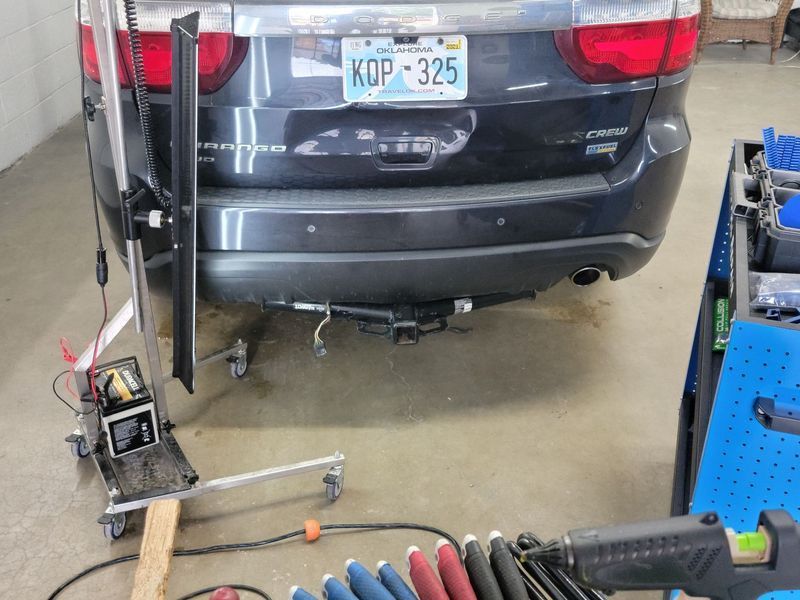 Car being repaired in a garage; dent in rear bumper, with auto body repair tools surrounding it.