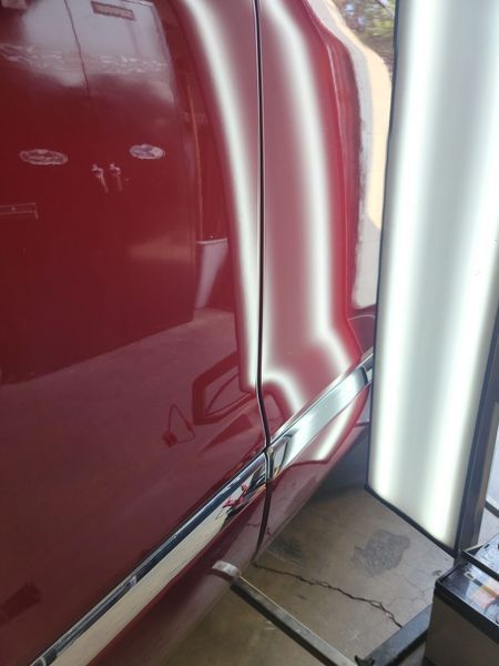 Red car door with a dent; a reflection board shows the damage.