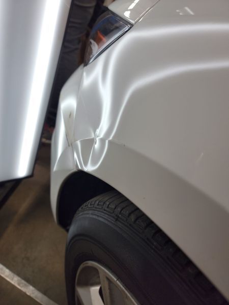 White car's rear quarter panel with a dent, reflecting bright light. Tire visible.