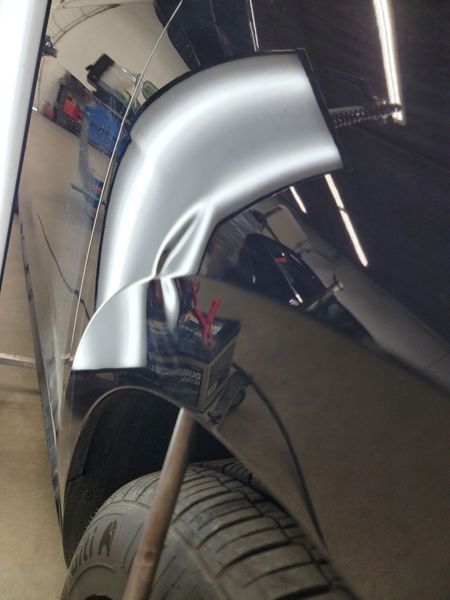 A black car fender with a significant dent being repaired using specialized tools.