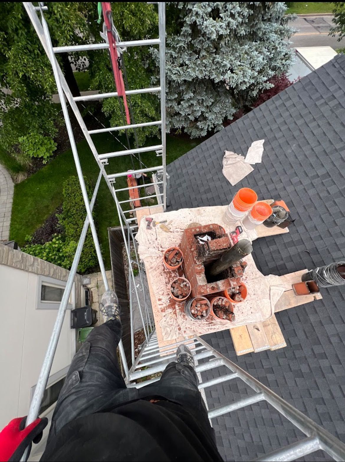 Person on scaffolding near a chimney, working on a roof with tools.