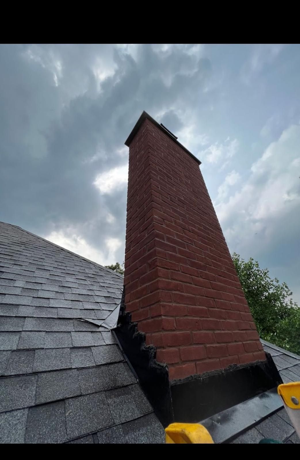 Brick chimney extending from a gray shingled roof against a cloudy sky.