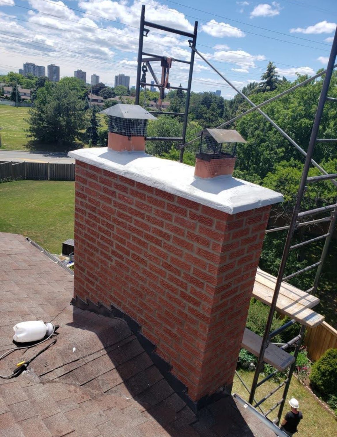 Brick chimney with two metal chimney caps on a rooftop; a construction scaffold is alongside.