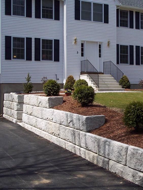 a white house with black shutters and a stone wall.
