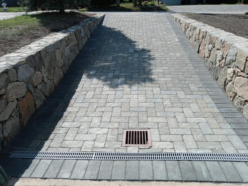 Stone driveway with brick pavers, rock walls, and drainage grate.