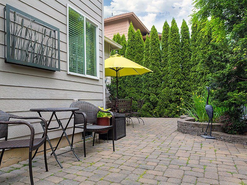 A patio with a table and chairs and a yellow umbrella.