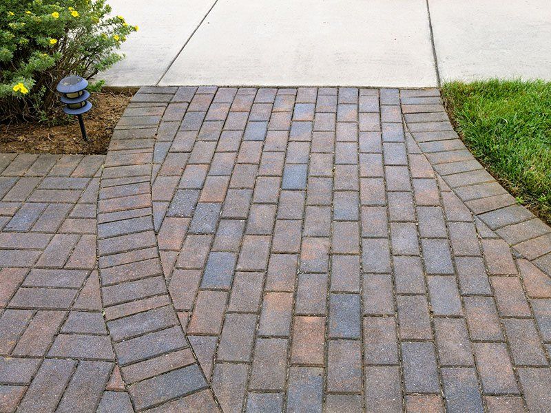 A brick walkway leading to a concrete sidewalk.