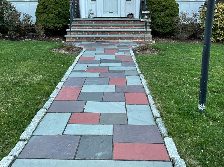 A colorful stone walkway leads to a house with a brick-lined entrance, flanked by green grass.