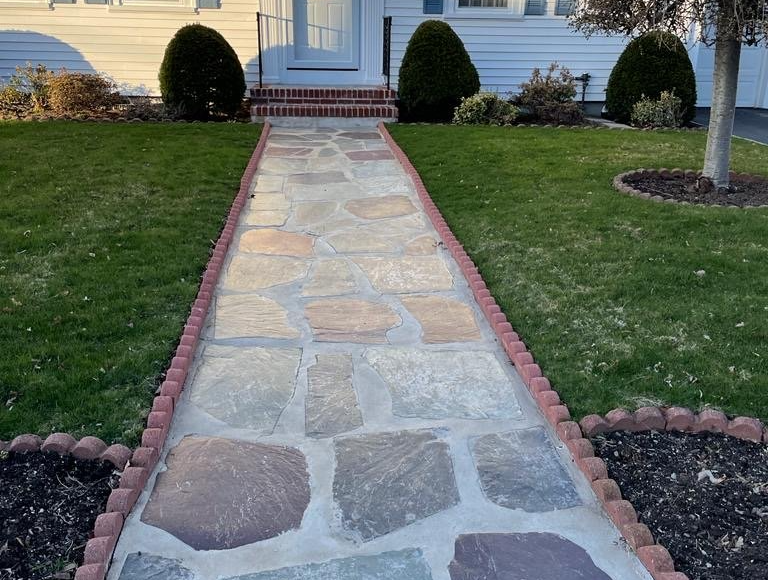 Stone walkway leading to a white front door, bordered by red bricks and green grass.