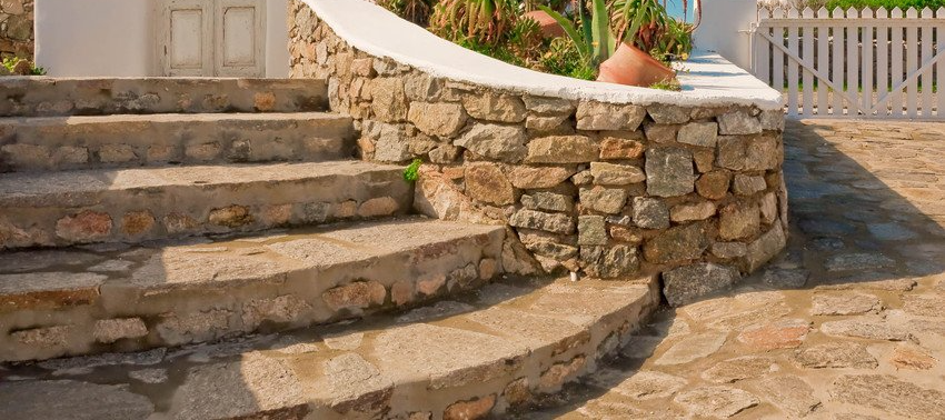 Stone steps leading up to a doorway, with a stone wall and white fence visible.