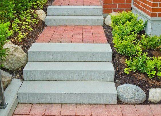 Concrete steps leading up to a building, surrounded by red brick walkway, plants, and rocks.