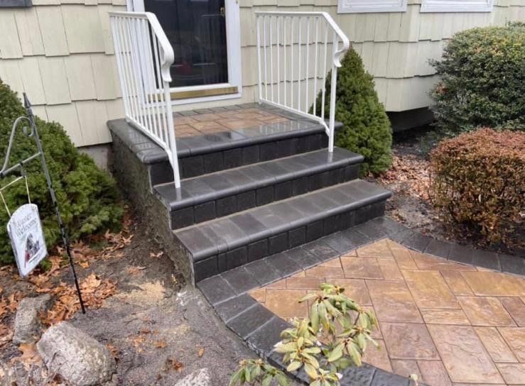 Dark gray brick steps leading to a front door with white railing, surrounded by landscaping.