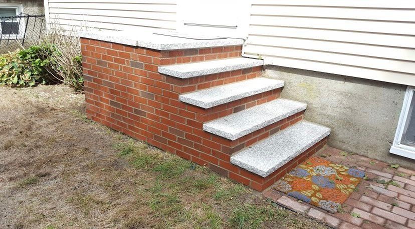 Brick steps with stone treads leading to a white door against a white-sided house.