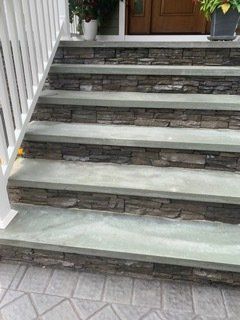 Stone steps leading to a door, featuring stacked stone risers and light gray treads with white railing.