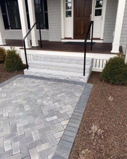 Gray brick walkway leading to steps and a front door with black handrails.
