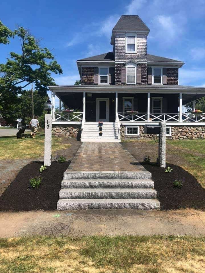 Two-story house with porch and stone steps leading to the front door. Mulch and small plants border the walkway.