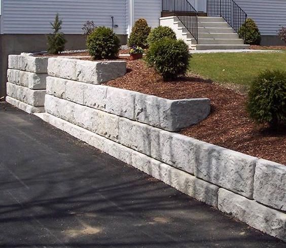 A stone wall surrounds a driveway in front of a house.
