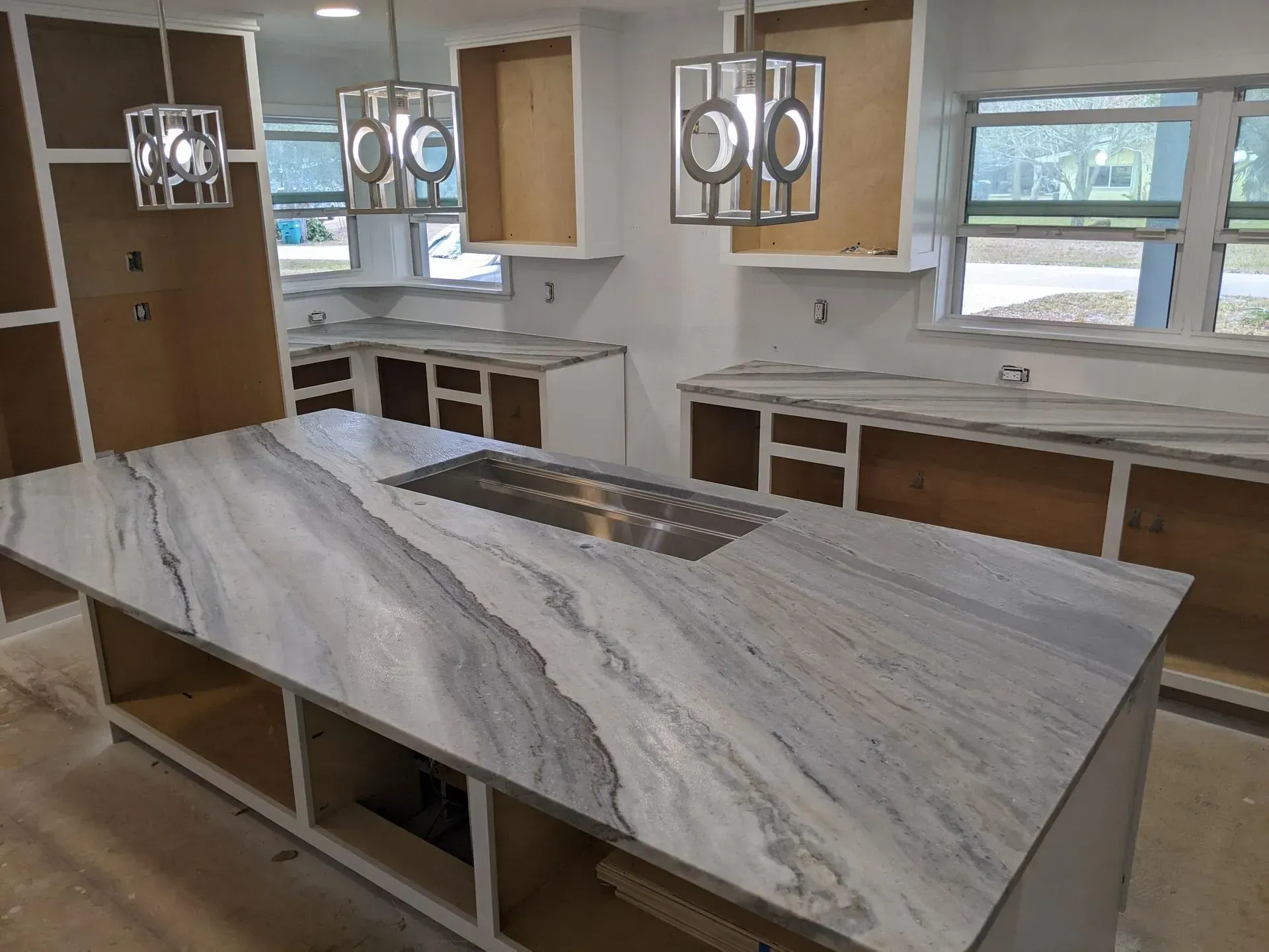 Modern kitchen with marble island, white cabinets, pendant lights, and large windows