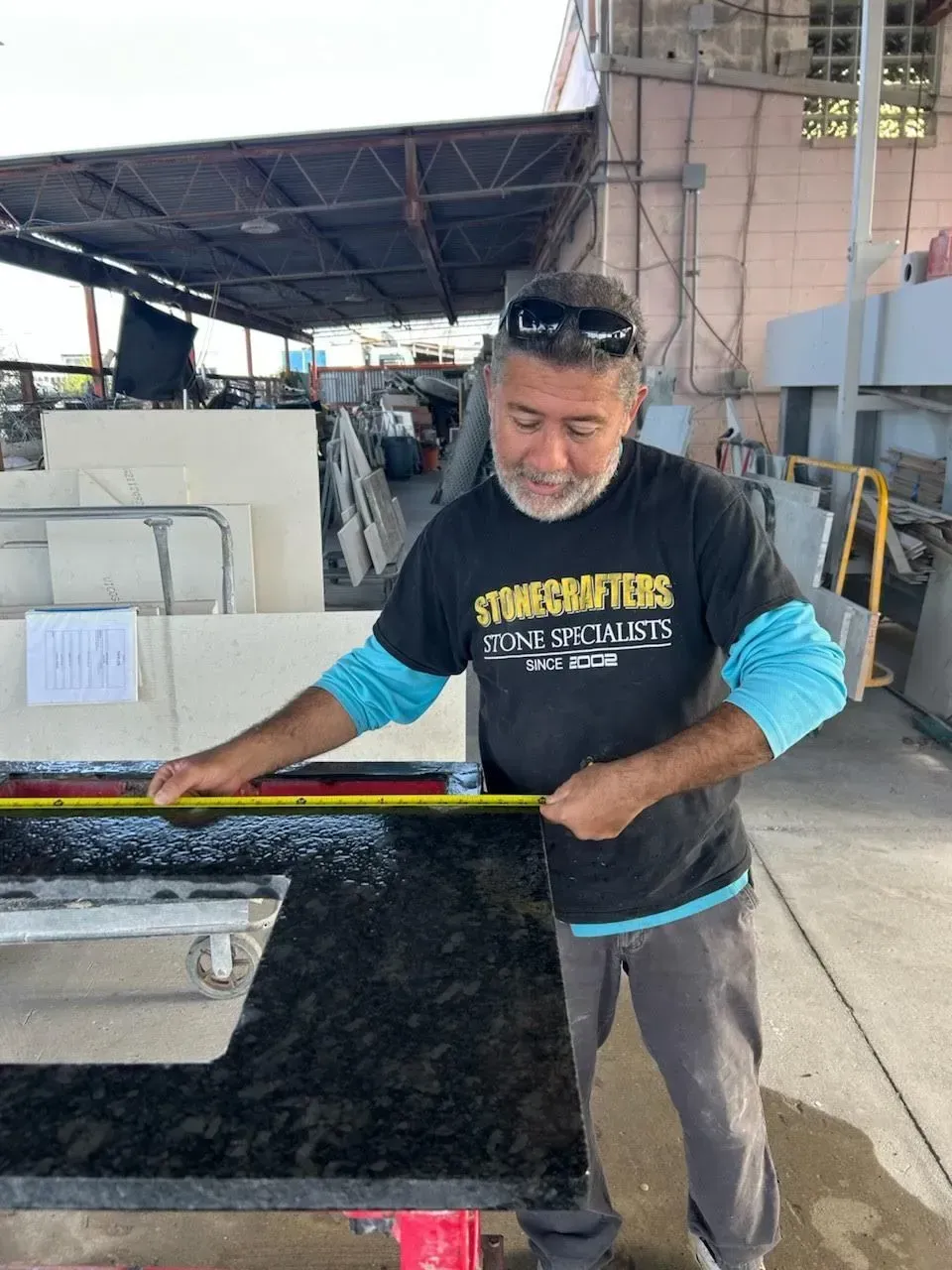 Man in a blue shirt and black vest working with a black barrier at an outdoor industrial site