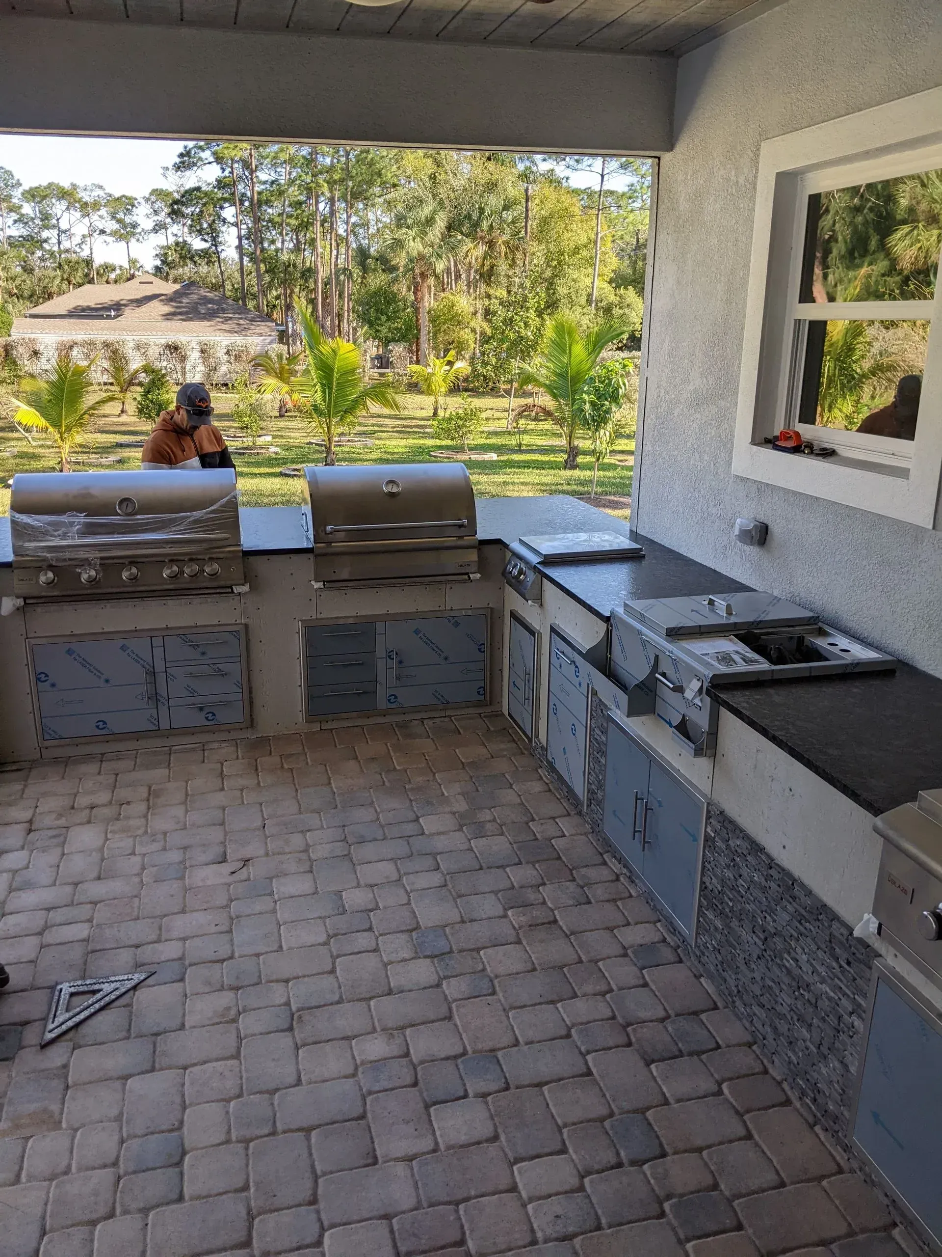 Outdoor patio kitchen with stone counters, grill, sink, and paver floor under a covered roof