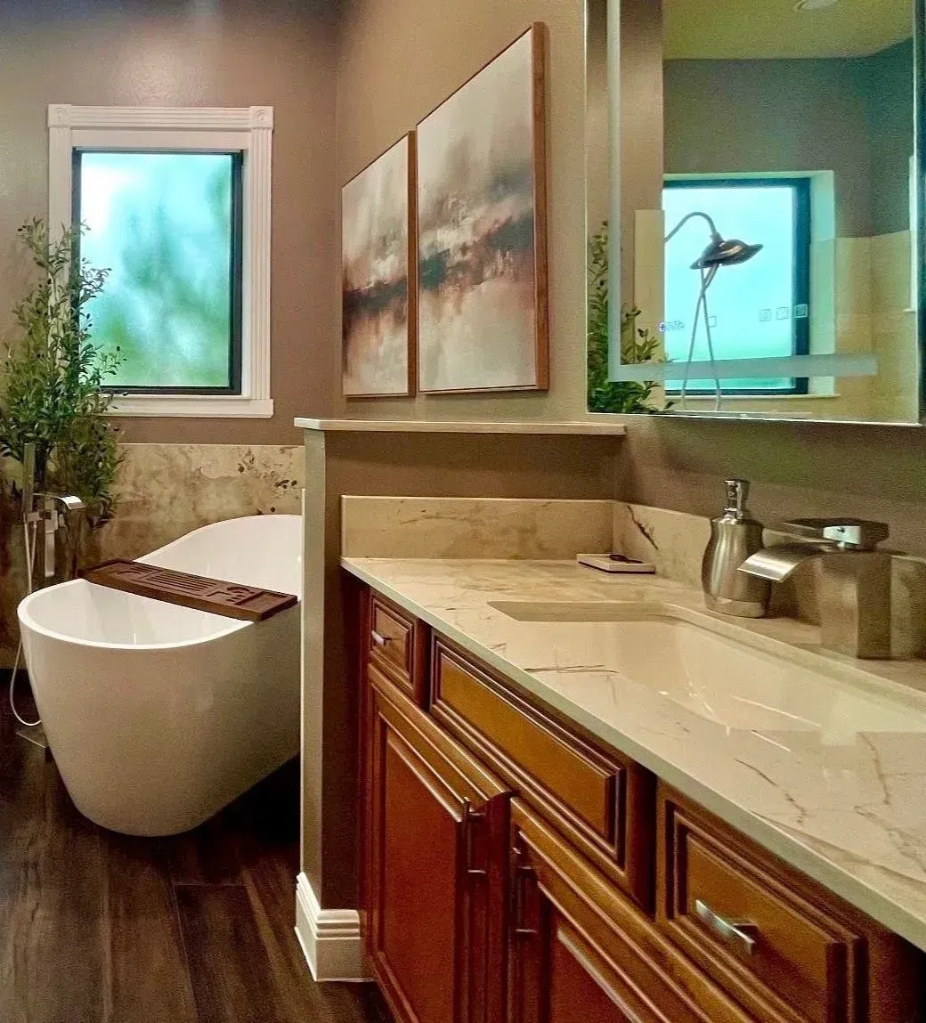 Modern bathroom with wooden vanity, marble countertop, sink, wall art, and freestanding tub by a window.
