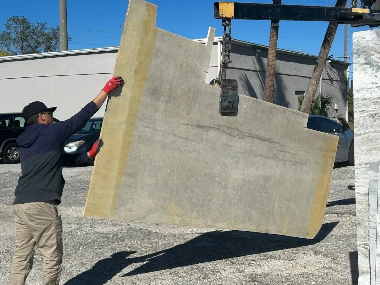 Worker guiding a large concrete wall panel suspended by a crane outdoors