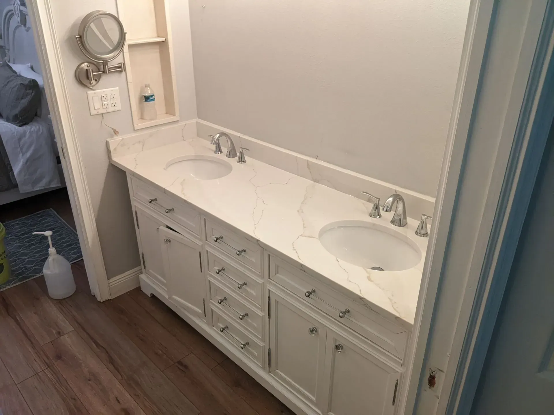 Bathroom vanity with double sinks, white countertop, and gray cabinets beside a mirror.