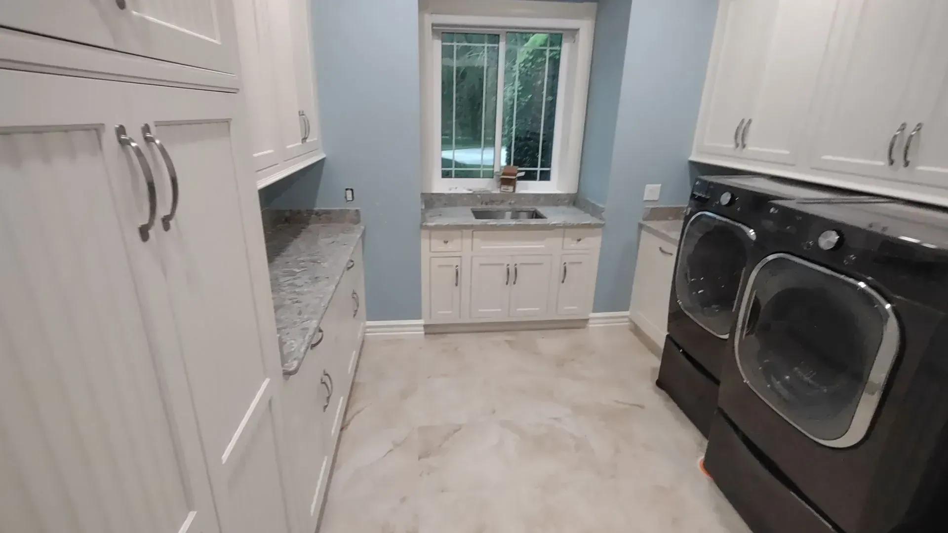 Bright laundry room with white cabinets, black washer and dryer, and a sink under a window.