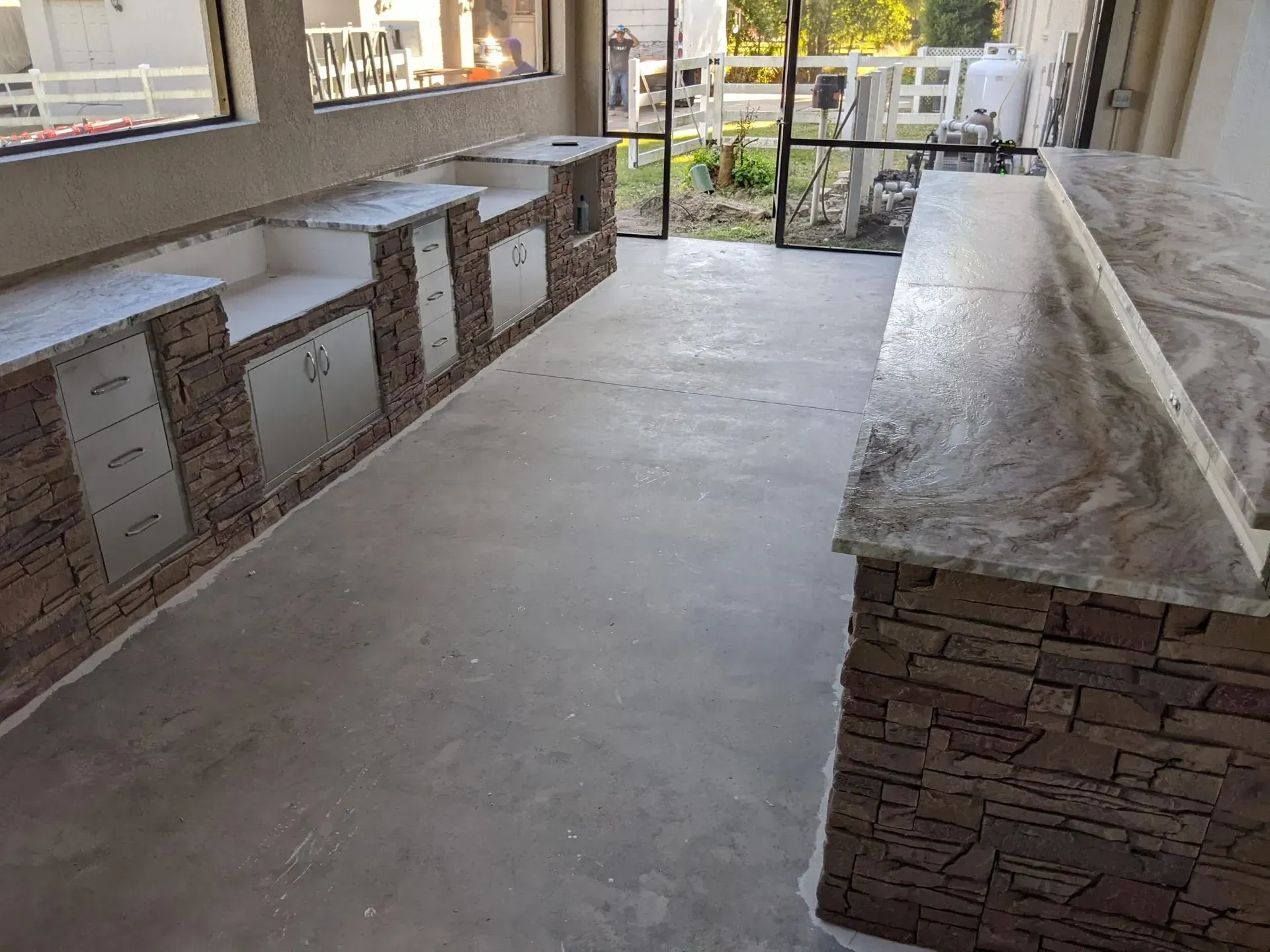Outdoor patio with built-in stone counters and a long stone bench beside a paved walkway.