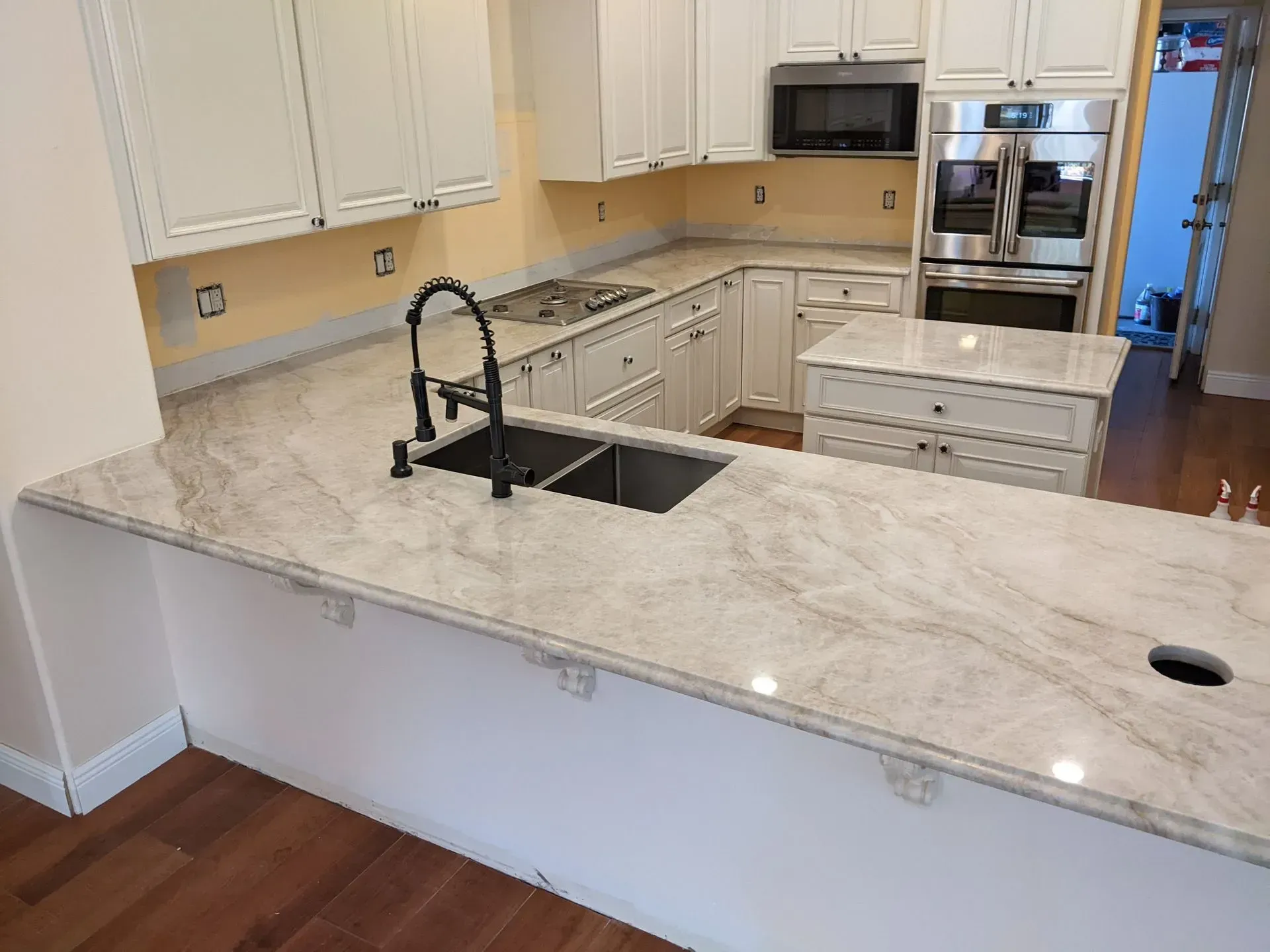 Bright white kitchen with marble island, black faucet, wood floor, and built-in appliances.