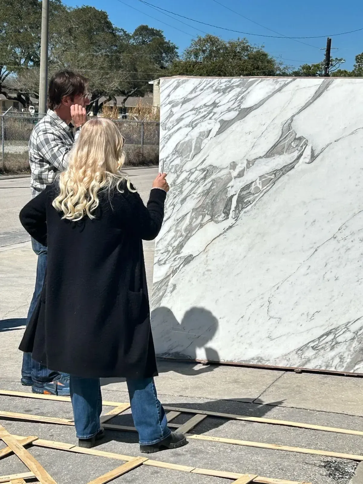Two people outdoors inspecting a large white marble slab on a pallet