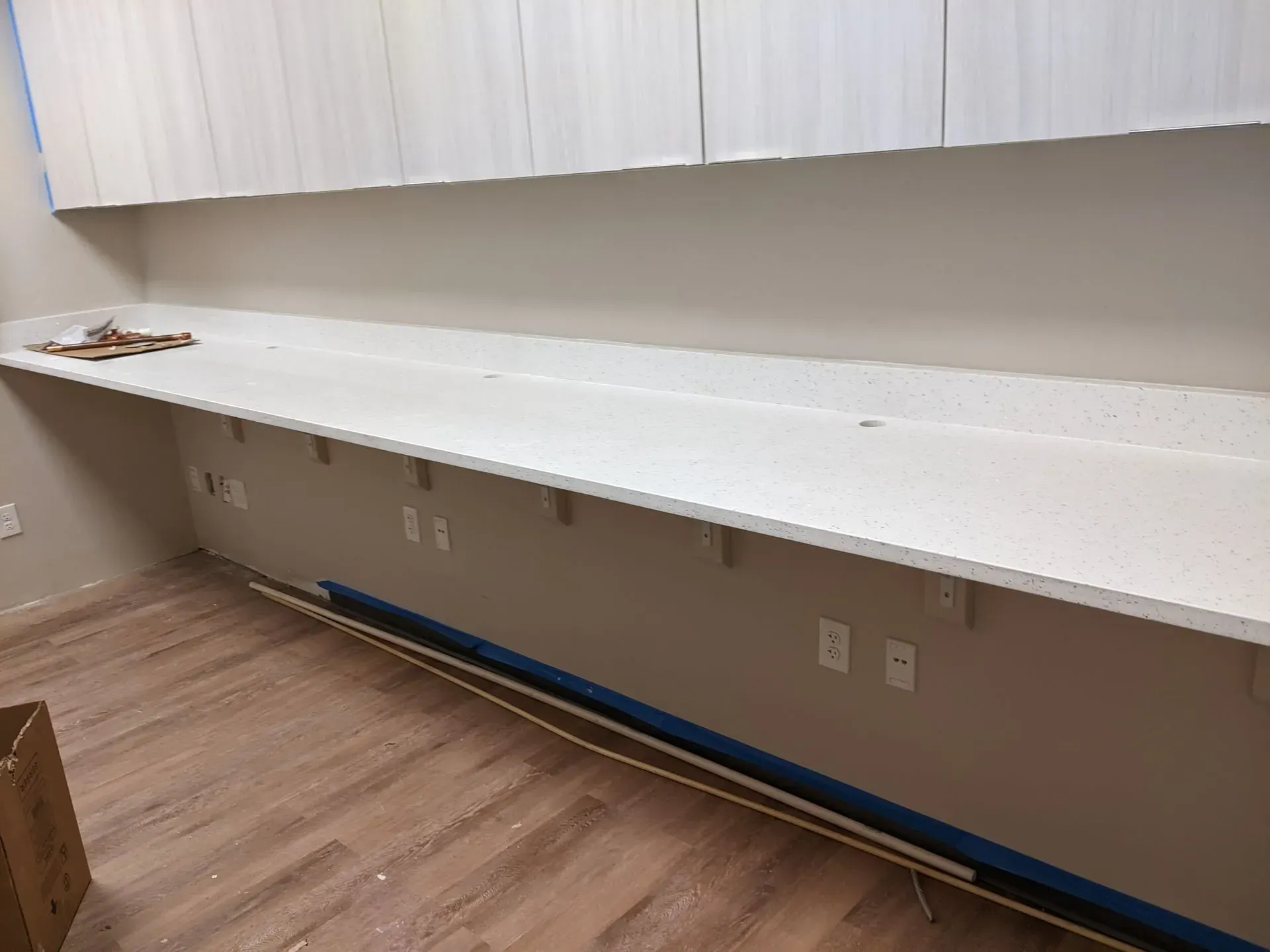 Empty office with a long white wall-mounted counter, cabinets above, and wood flooring.