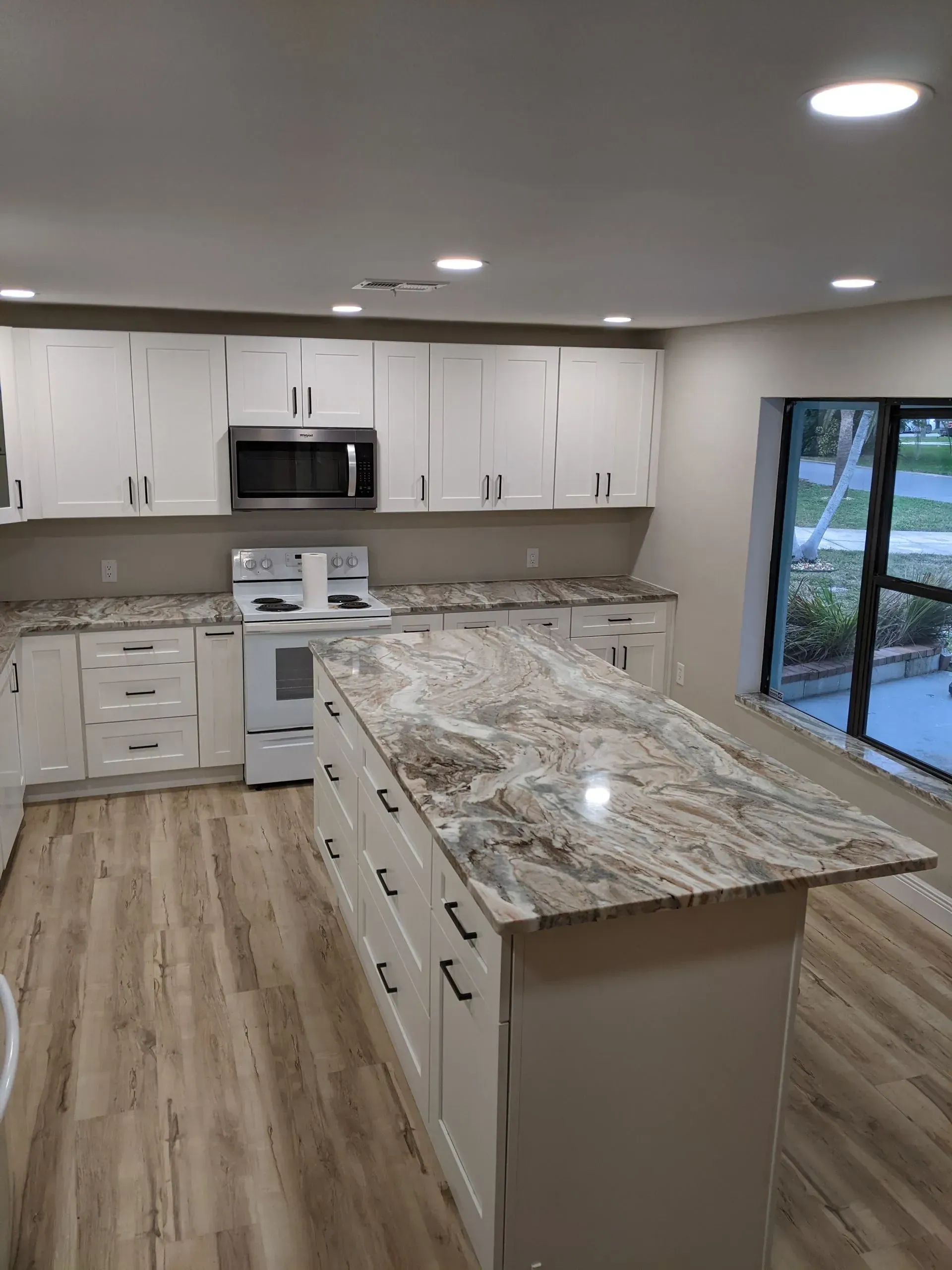 Bright modern kitchen with white cabinets, granite island, stainless appliances, and sliding glass doors.