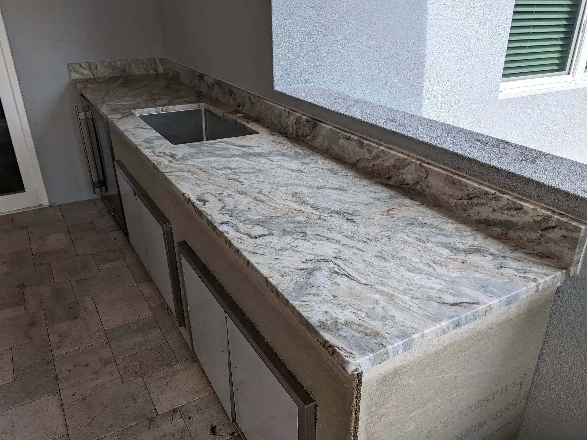 Long stone outdoor counter with a built-in sink and marble-patterned top in a patio area