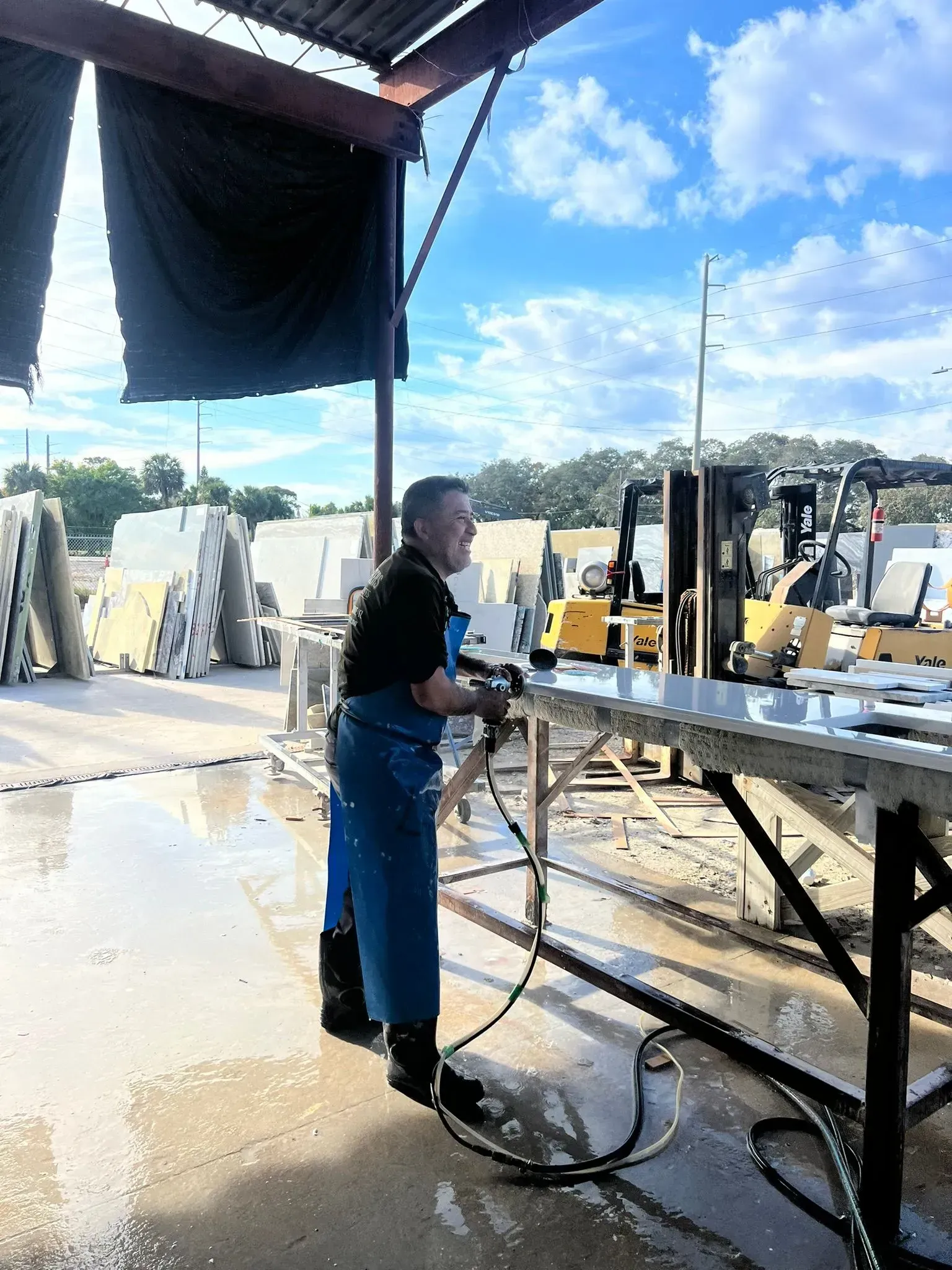 Person washing a metal table at an outdoor worksite with water hose and wet floor
