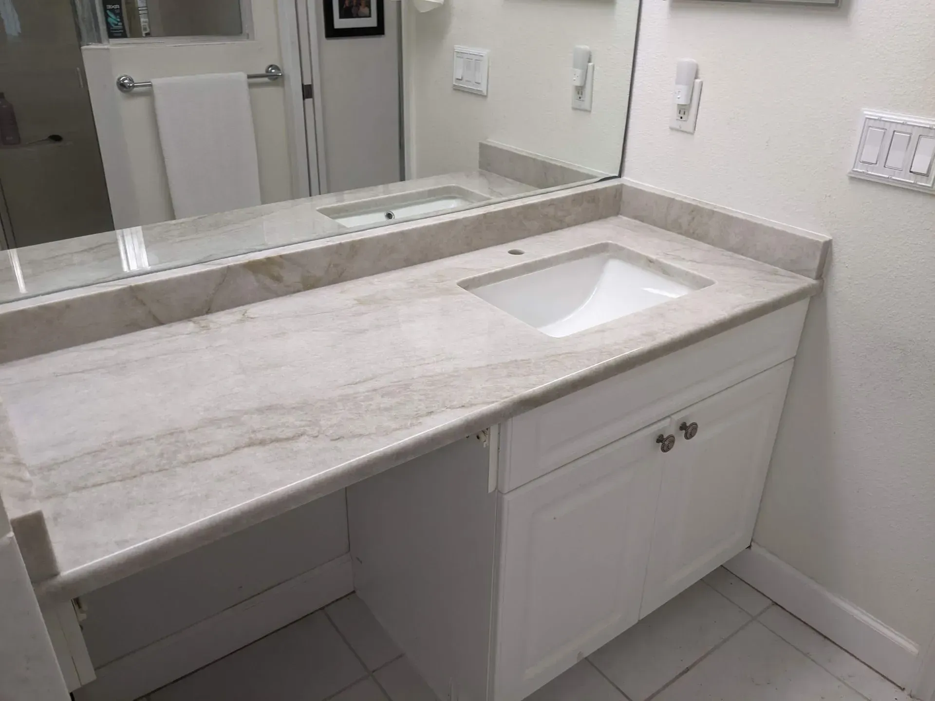 White bathroom vanity with built-in sink, light stone countertop, and large mirror.