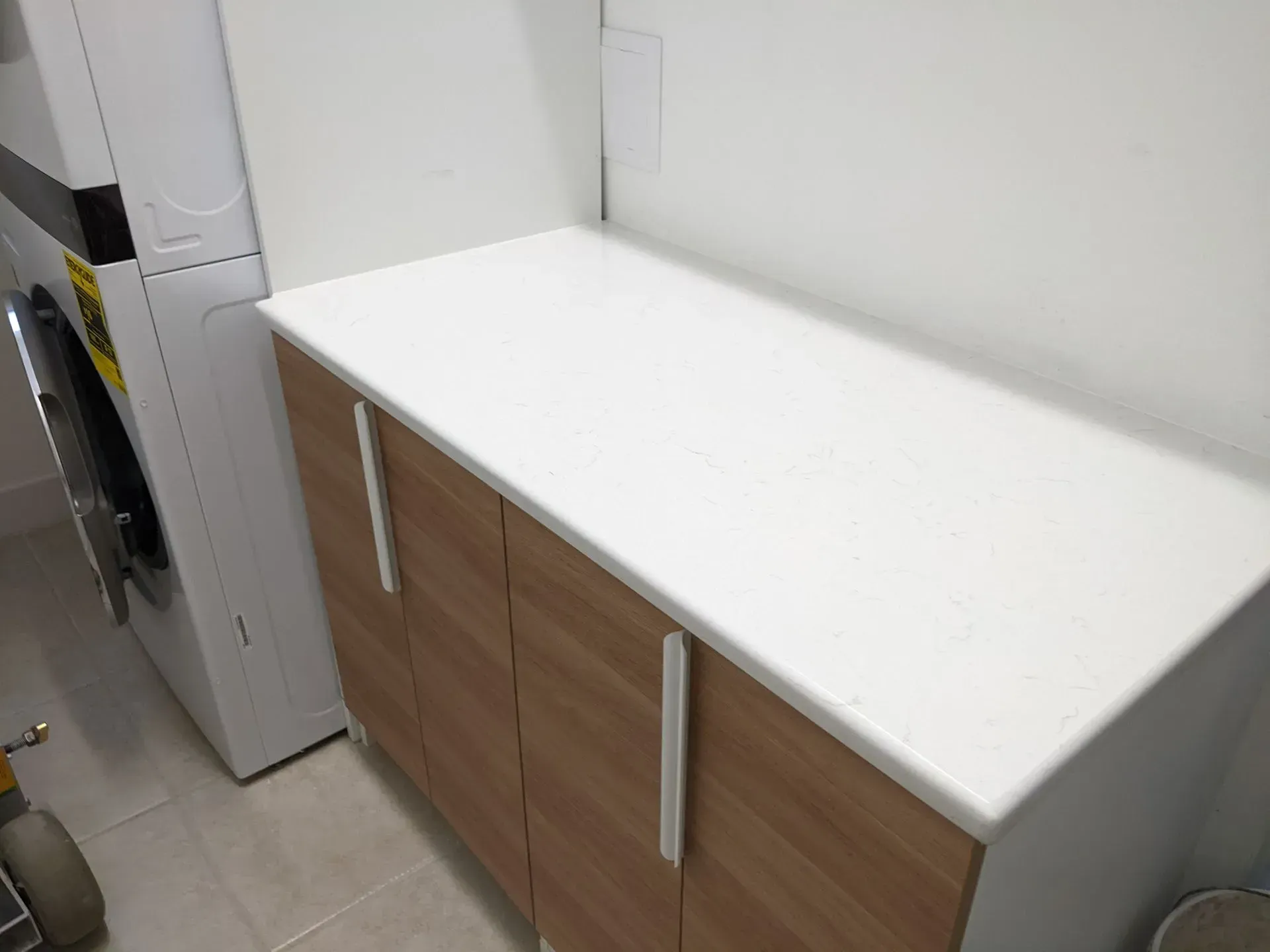 White countertop above wood cabinets in a small kitchen or utility room