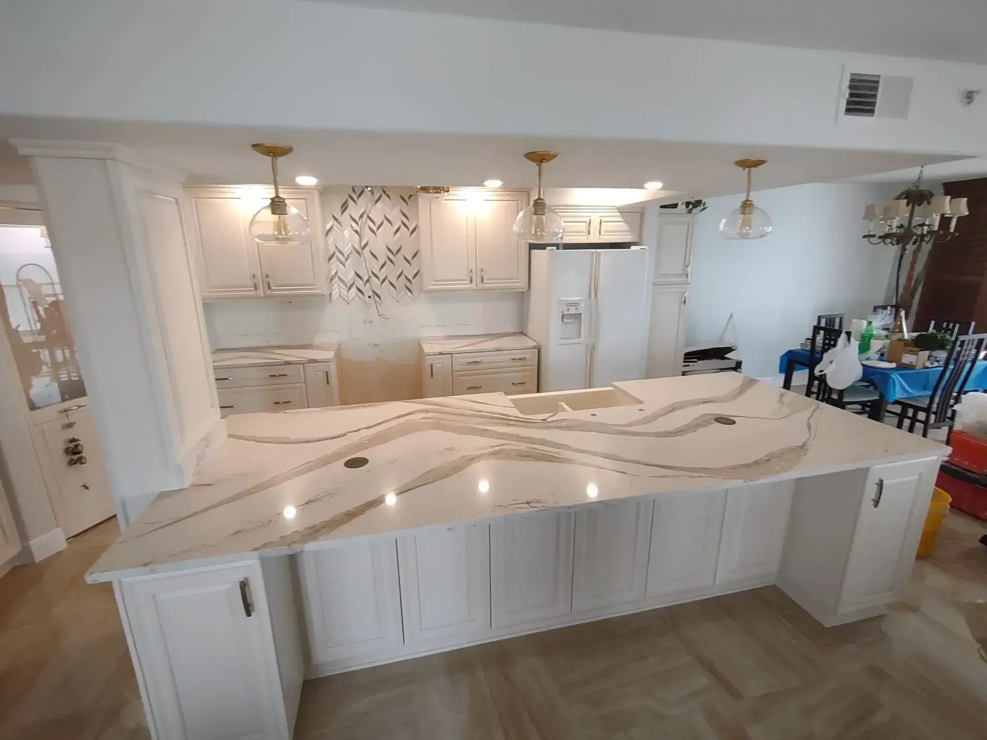 Bright kitchen with a large marble island, white cabinets, and pendant lights under a vaulted ceiling