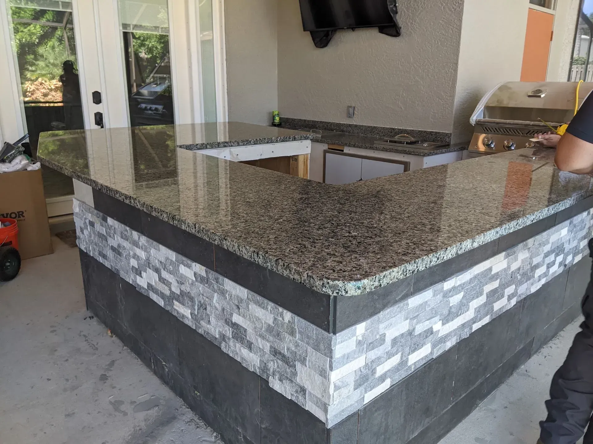 Outdoor kitchen island with speckled granite countertop and gray stacked-stone base under a covered patio