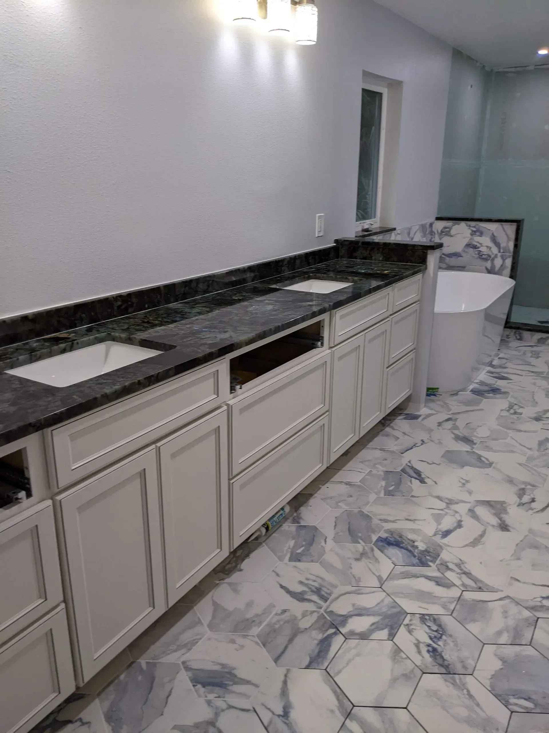 Long bathroom vanity with black countertop, white cabinets, and blue-white patterned floor tiles