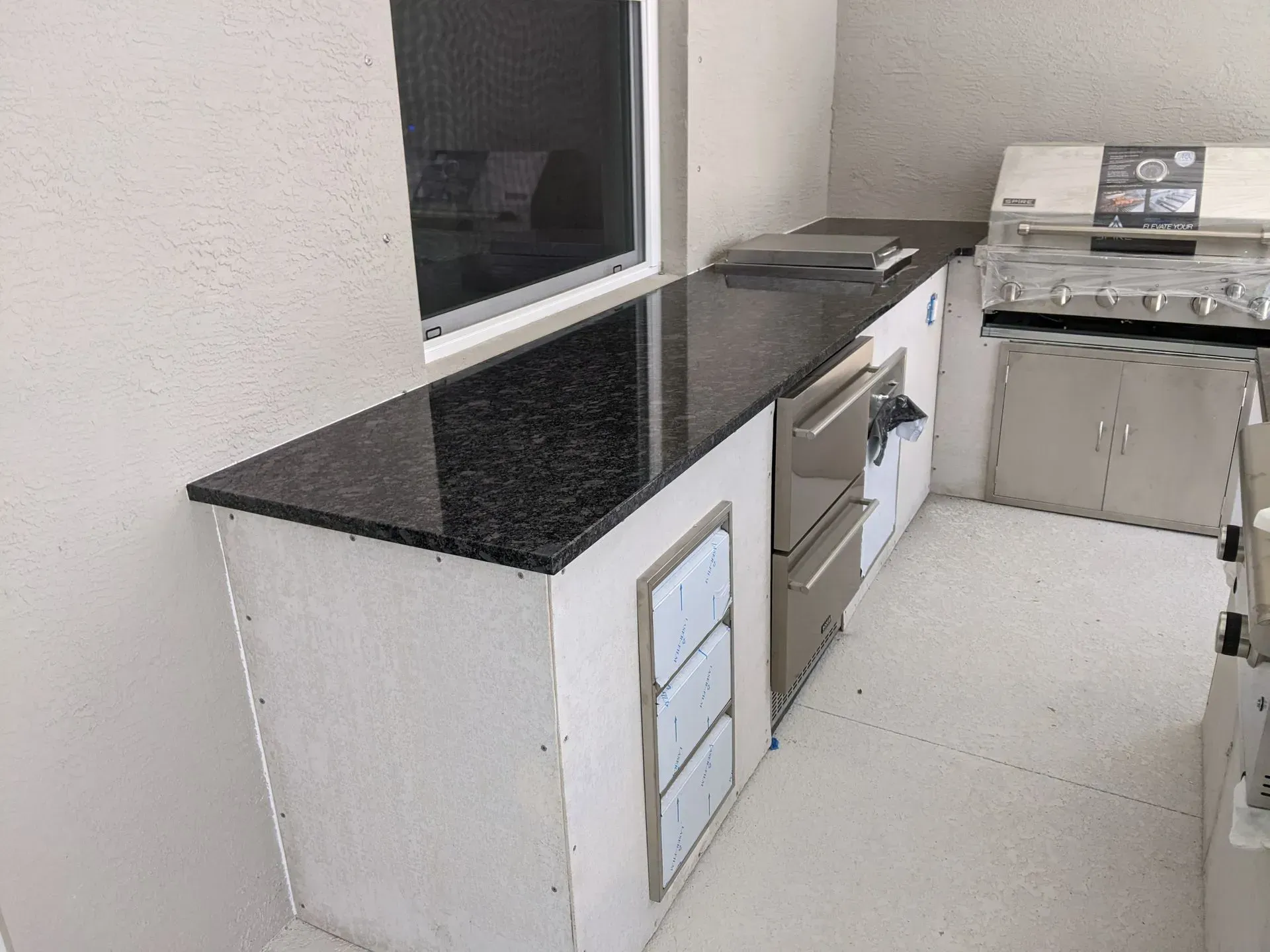 Modern kitchen with black granite counters, white cabinets, and a gas stove near a window.