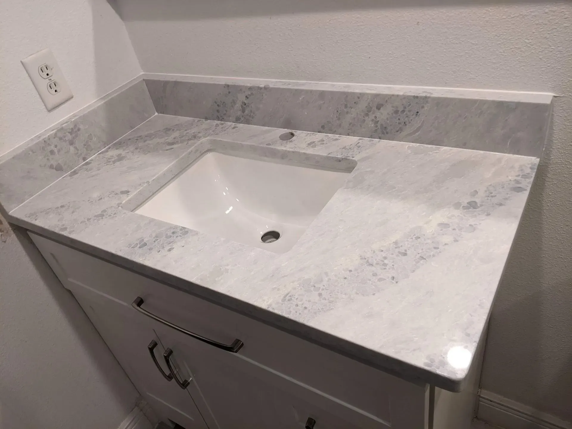 Bathroom vanity with light gray marble countertop and integrated sink, viewed at an angle.