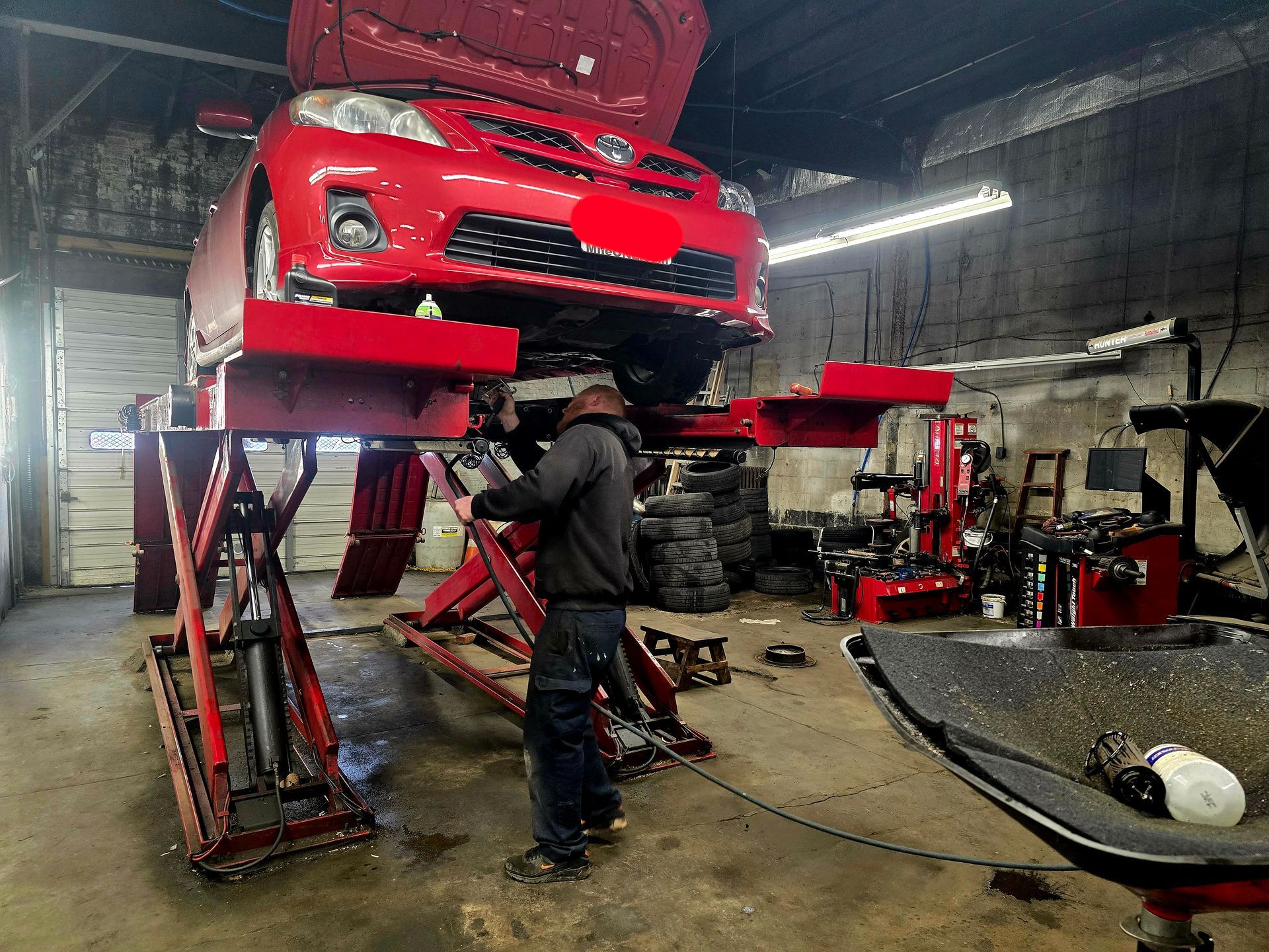 A man is working on a red car on a lift in a garage.