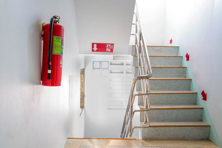 Stairwell with white walls, a red fire extinguisher, and stairs leading up on the right.
