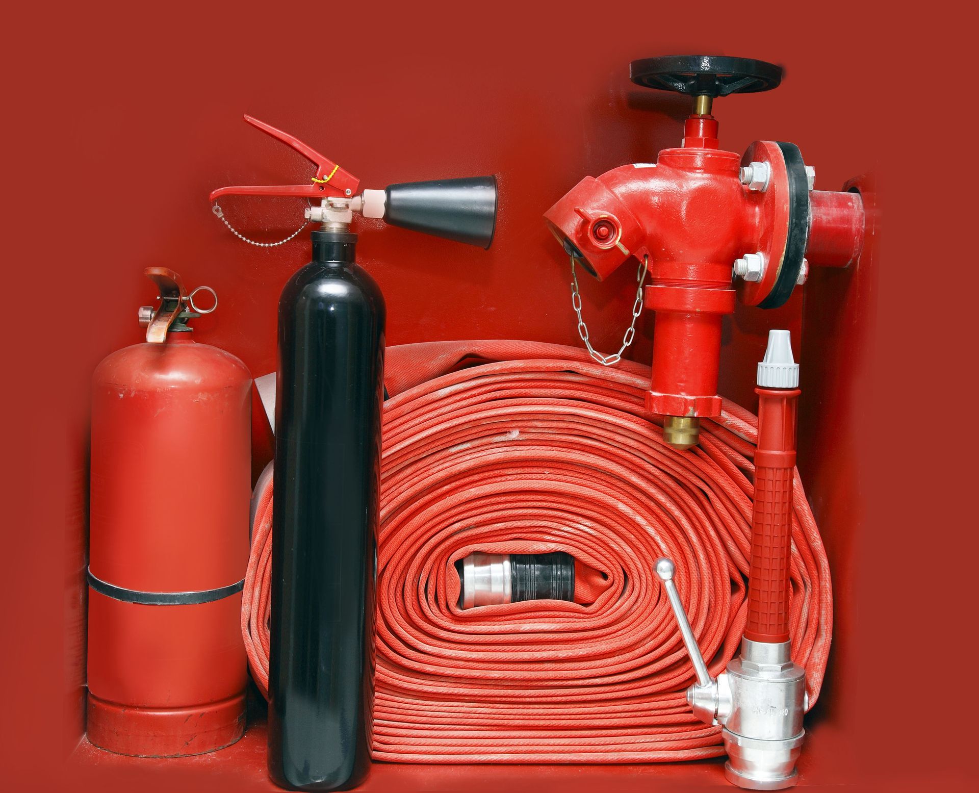 Red fire safety equipment: extinguisher, hose reel, helmet, and fire hoses on a red background
