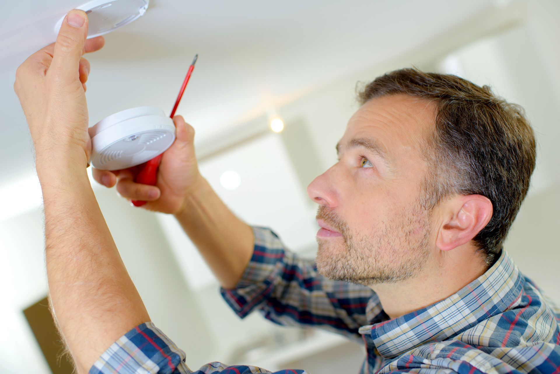Man painting a ceiling with a red paint roller in a bright room