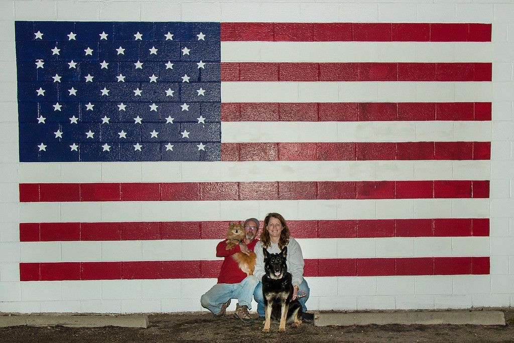Two people and a dog standing in front of an american flag