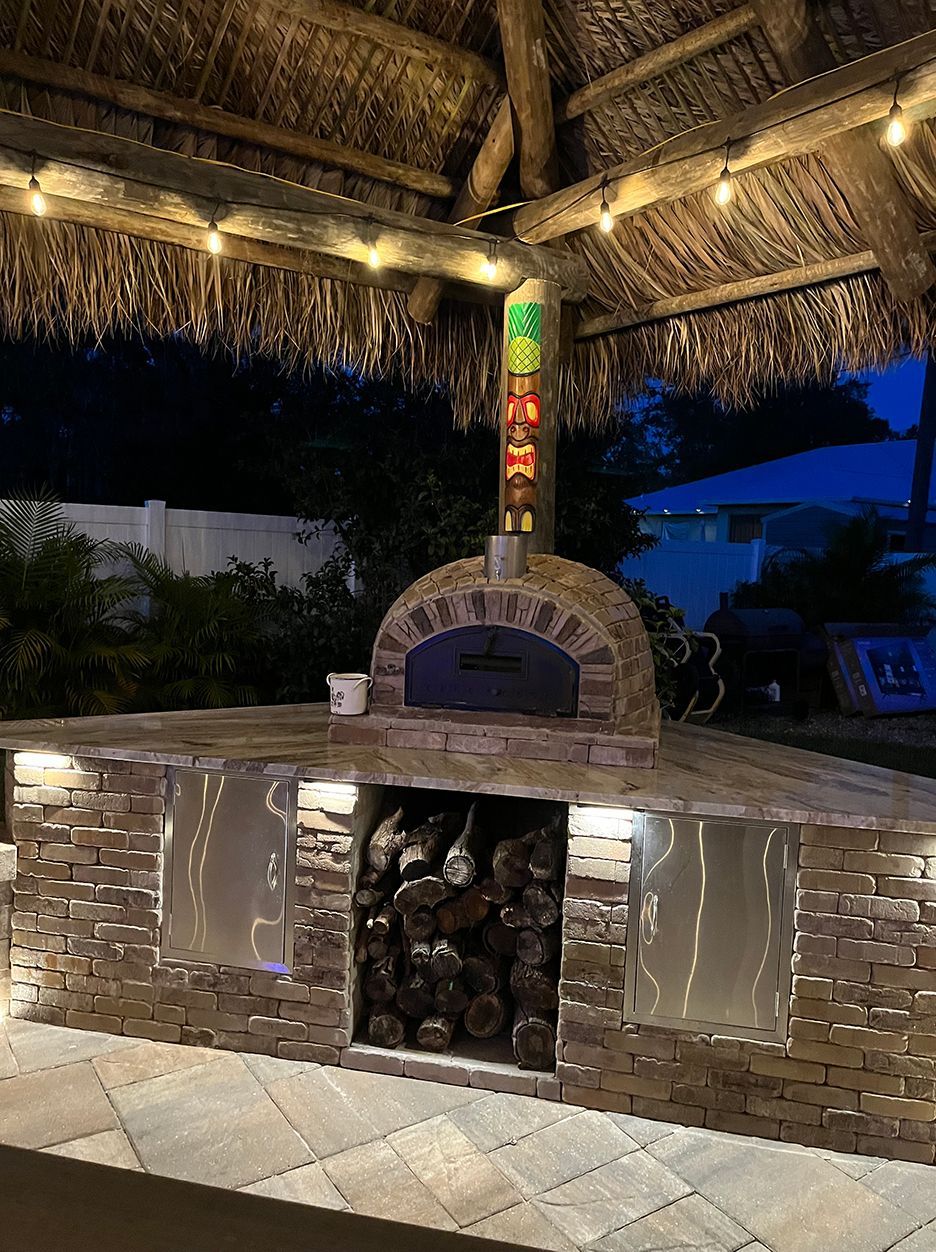 A pizza oven is sitting under a thatched roof.