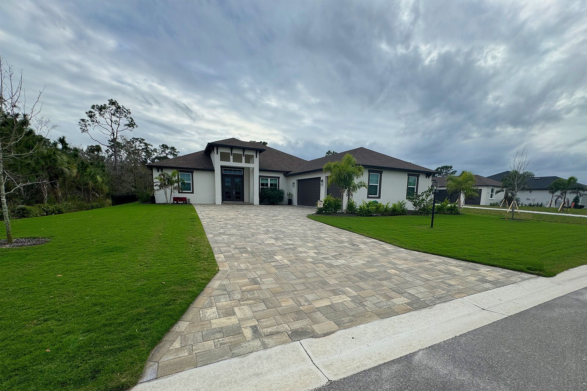 A large white house with a brick driveway and a lush green lawn.